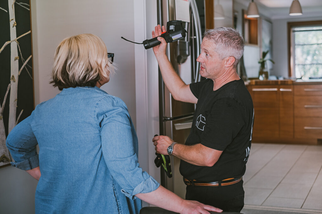 Imagine Inspection owner dressed in black, holding a thermal camera and explaining details to a female client wearing blue